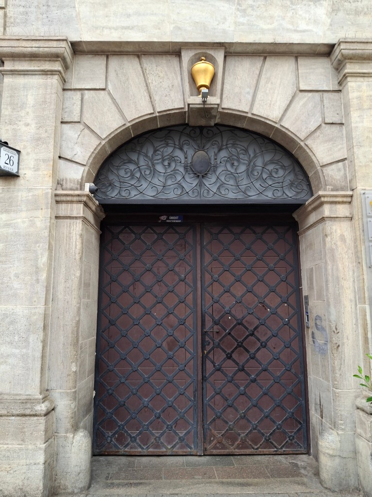 An ornate entrance with a decorative metal gate and an arched stone frame, featuring a wall-mounted light fixture above.