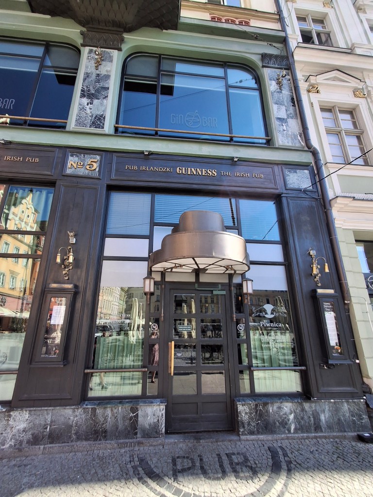 Entrance of an Irish pub with a black facade, large windows, and decorative elements. The pub features signage indicating it serves Guinness.