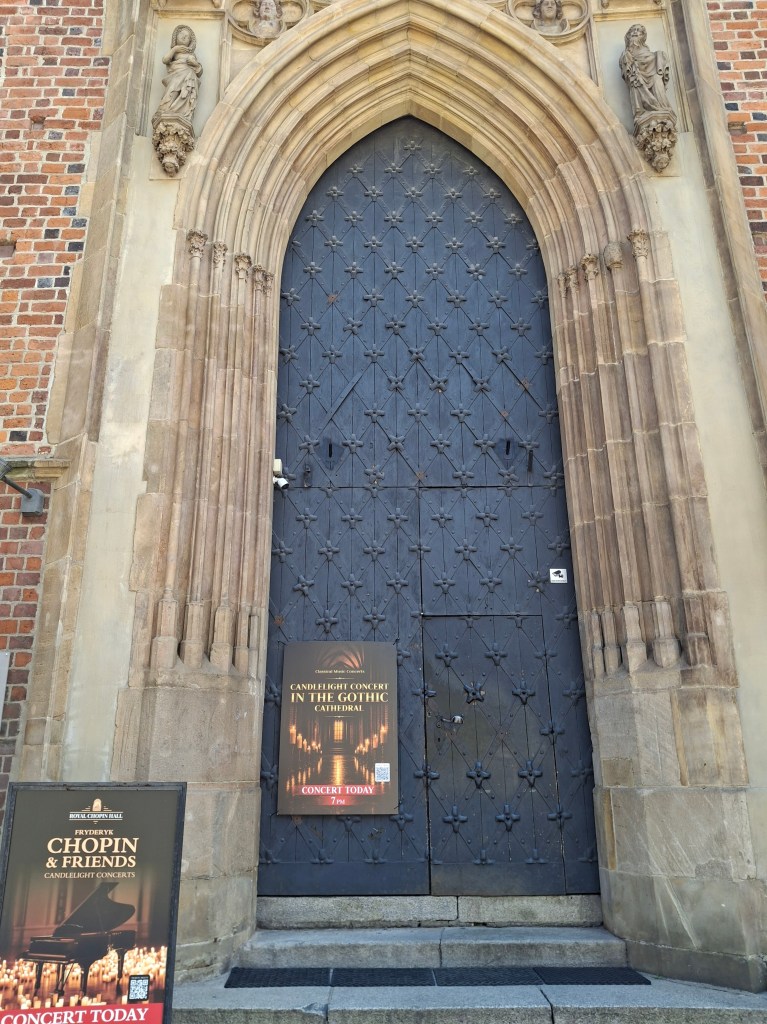 Gothic cathedral door with ornate design and statues, featuring a concert poster for a Chopin and Friends candlelight concert.