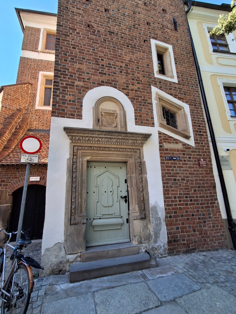 A historic building featuring a decorative stone doorway with an ornate arch, surrounded by red brick walls, and a bicycle parked nearby.